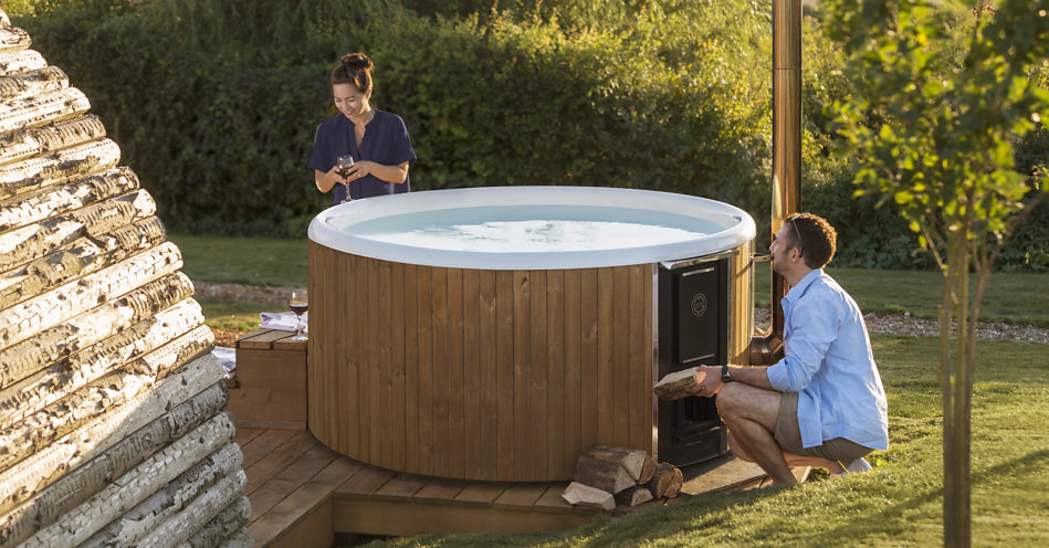A man firing up the hot tub while the woman stands on the other side and holds a glas in her hands.
