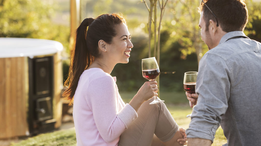 A man and a women holding a glas in their hand. In the background a hot tub is placed.